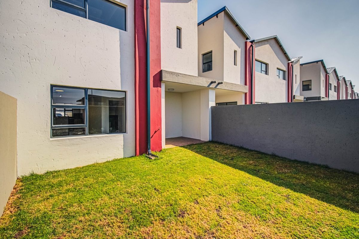 Rear view of a modern townhouse featuring a small private garden, a covered patio area, and a secure boundary wall.