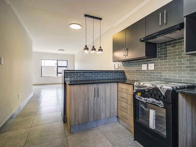 Modern open-plan kitchen featuring dark cabinetry, subway tile backsplash, granite countertops, and a built-in oven, flowing into a spacious living area.