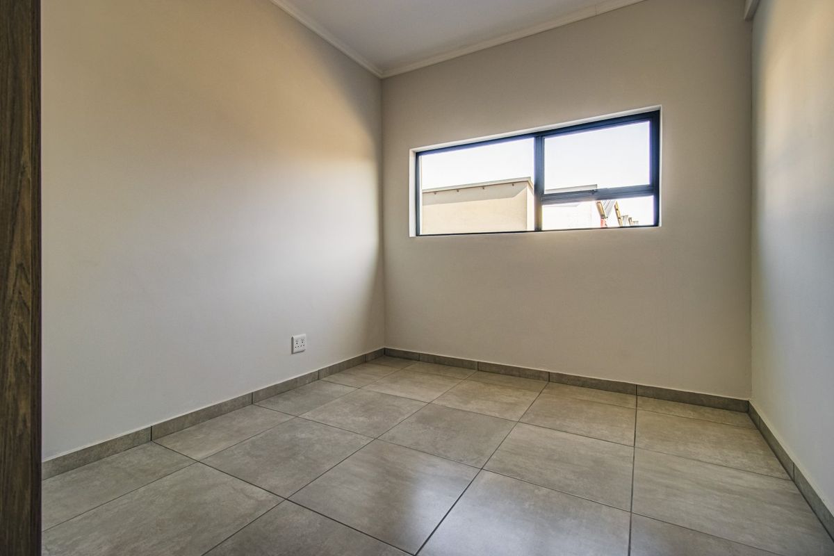 A clean, empty bedroom featuring neutral tiled flooring, smooth walls, and a modern aluminium-framed window providing natural light.