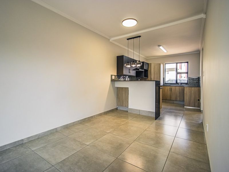 An open-plan kitchen area featuring modern cabinetry, a breakfast bar, tiled flooring, and neutral finishes, offering a clean and functional space.