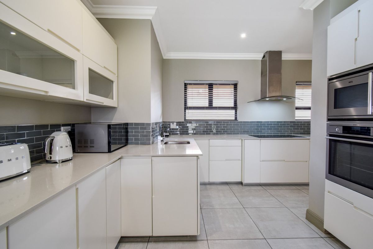 Modern kitchen featuring sleek white cabinetry, stone countertops, subway tile backsplash, and high-quality integrated stainless steel appliances.