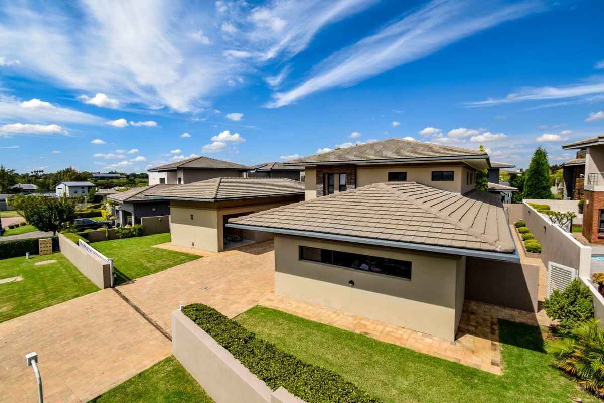 Aerial view of a modern residential property featuring a tiled roof, paved driveway, and well-maintained landscaped garden areas.