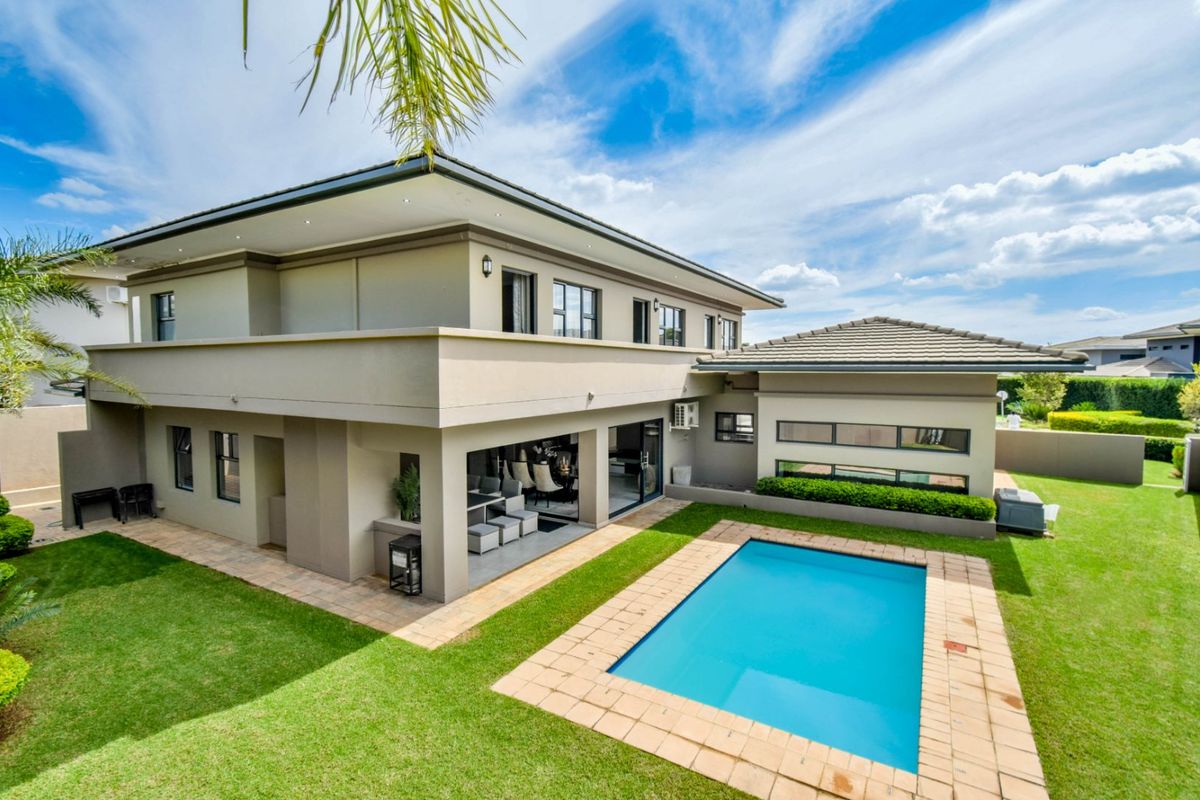 Rear view of a modern double-story house featuring a covered patio, a well-maintained swimming pool, and a landscaped garden.