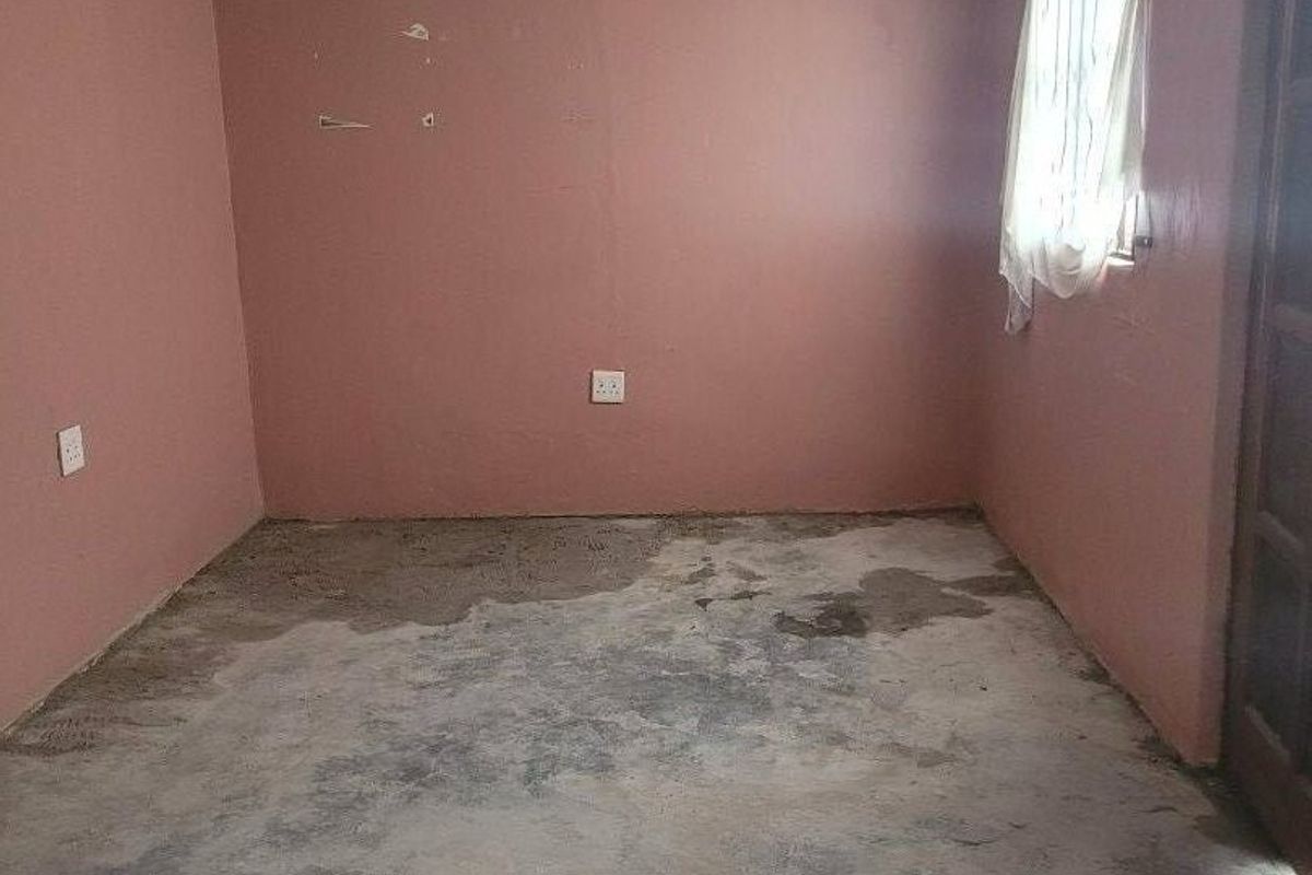 An empty bedroom featuring unfinished concrete flooring and pink walls requiring cosmetic attention and new floor finishes.