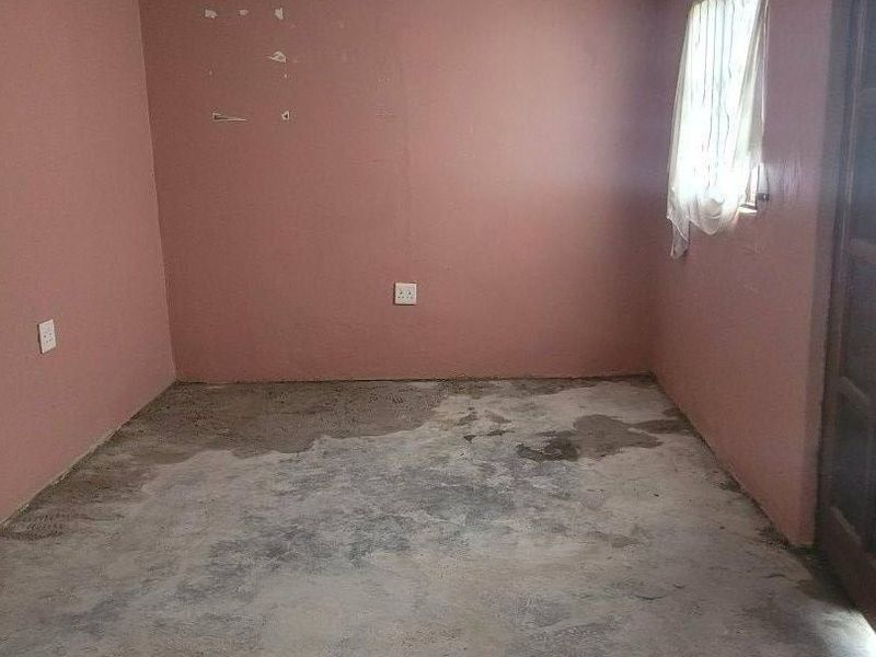 An empty bedroom featuring unfinished concrete flooring and pink walls requiring cosmetic attention and new floor finishes.