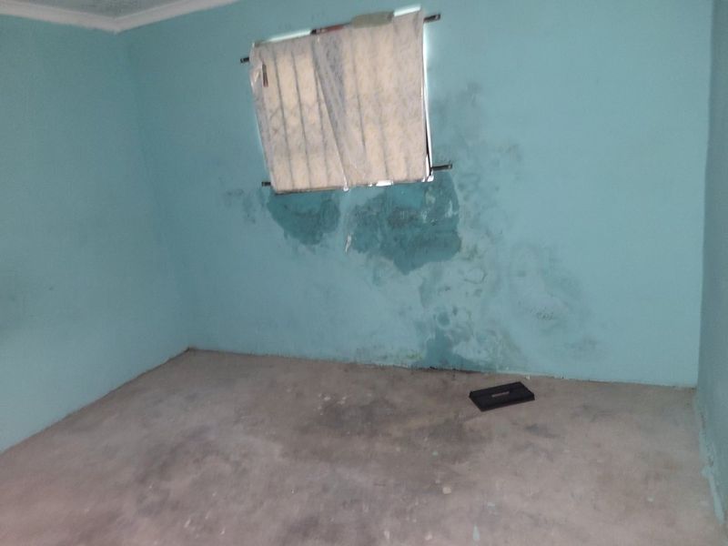 An empty bedroom featuring unfinished concrete flooring and significant visible damp damage on the walls requiring repair and refurbishment.