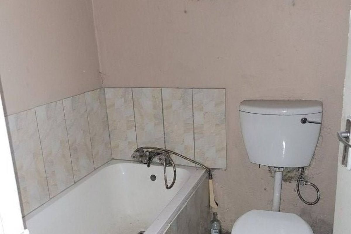 A compact bathroom featuring a bathtub, toilet, tiled flooring, and tiled splashback, requiring cosmetic updates and repairs to wall finishes.