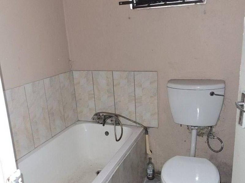 A compact bathroom featuring a bathtub, toilet, tiled flooring, and tiled splashback, requiring cosmetic updates and repairs to wall finishes.