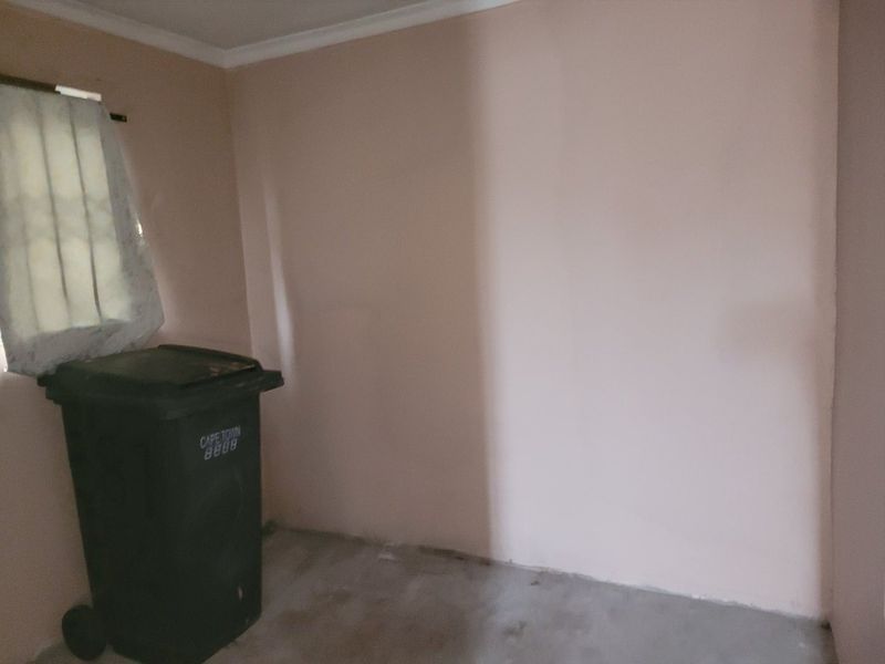 An empty, unfinished bedroom space featuring plain walls, a window with security bars, and an exposed concrete floor.