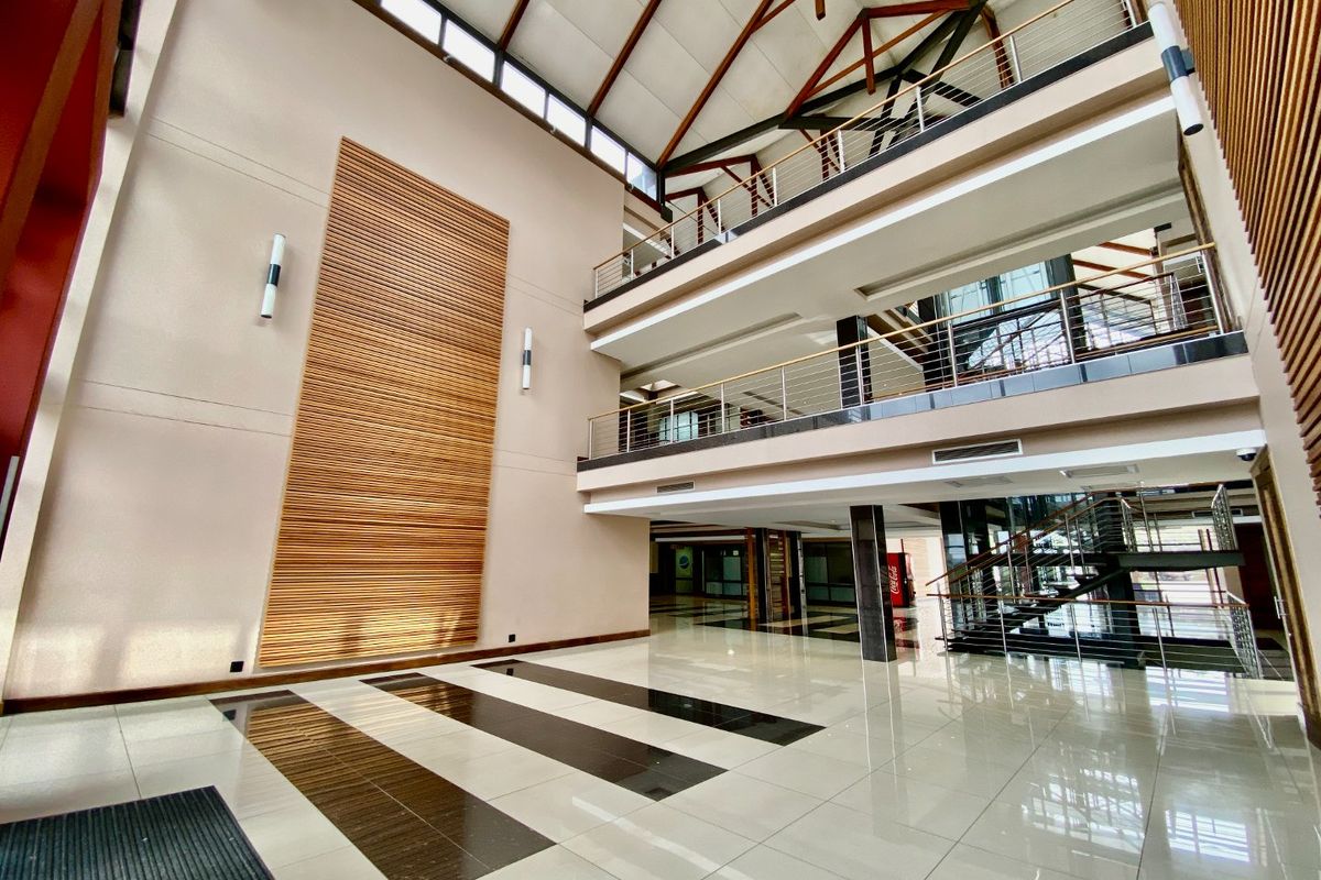 Spacious commercial atrium featuring a high vaulted ceiling with exposed timber trusses, polished tiled floors, and a modern multi-level mezzanine with stainless steel balustrades.