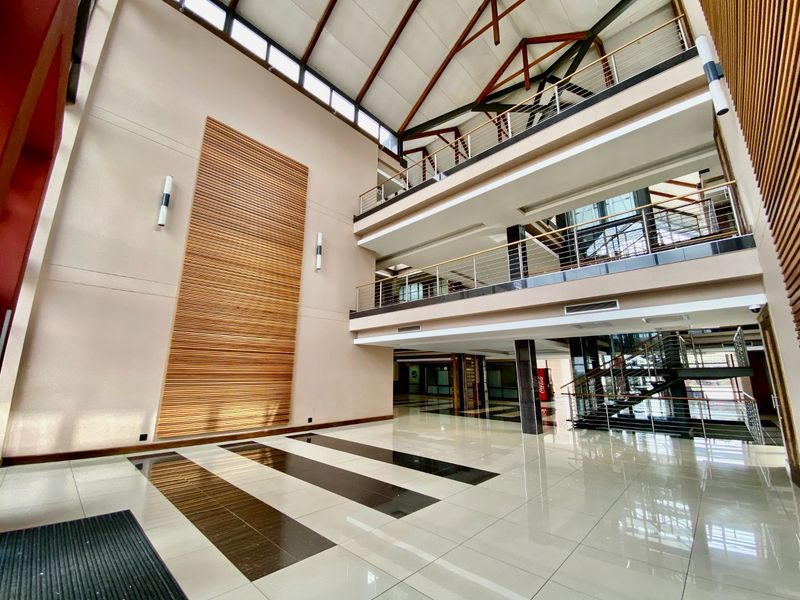 Spacious commercial atrium featuring a high vaulted ceiling with exposed timber trusses, polished tiled floors, and a modern multi-level mezzanine with stainless steel balustrades.