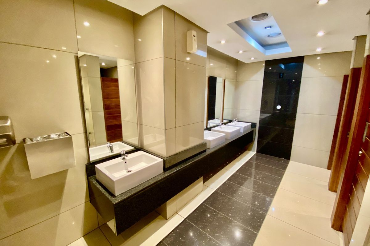 Modern commercial bathroom featuring three vessel sinks, granite vanity countertops, polished tile flooring, and recessed ceiling lighting.