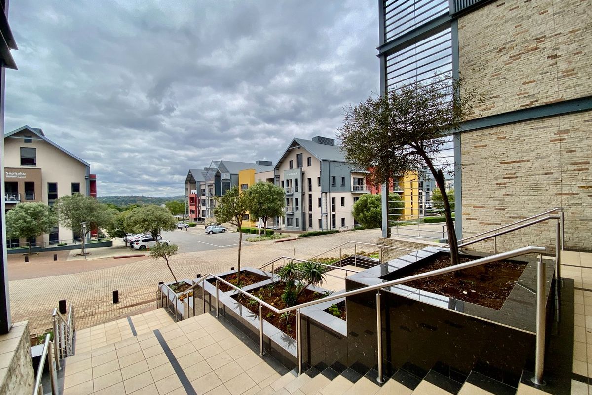 A view of a modern commercial office park featuring stone-clad building facades, paved walkways, landscaped planter boxes, and stainless steel staircase railings.