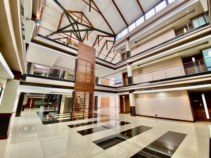 Spacious commercial atrium featuring a high vaulted ceiling with exposed timber trusses, multi-level mezzanine walkways, and modern tiled flooring.
