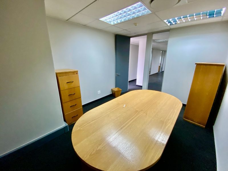 A functional office space featuring a suspended ceiling with recessed lighting, dark carpeting, and access to a connecting hallway.