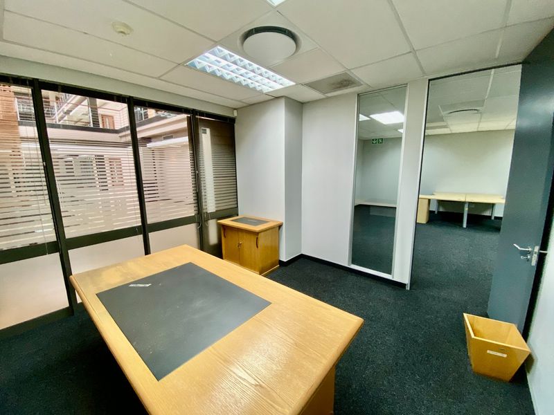 A functional commercial office space featuring glass partitions, suspended ceilings with recessed lighting, and carpeted flooring, offering a clean and professional work environment.