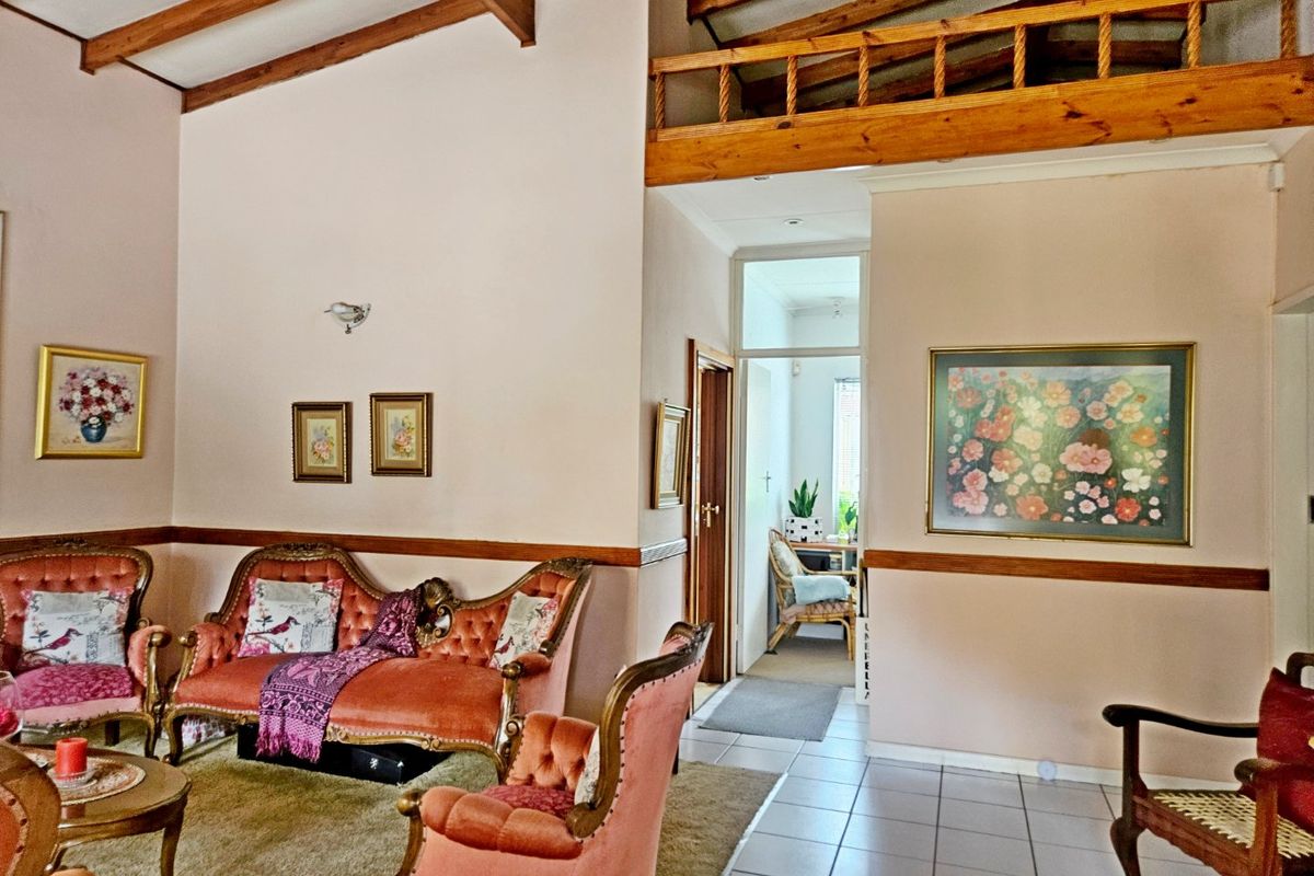 Spacious living area featuring high vaulted ceilings with exposed timber beams, a mezzanine loft level, and ceramic tiled flooring.