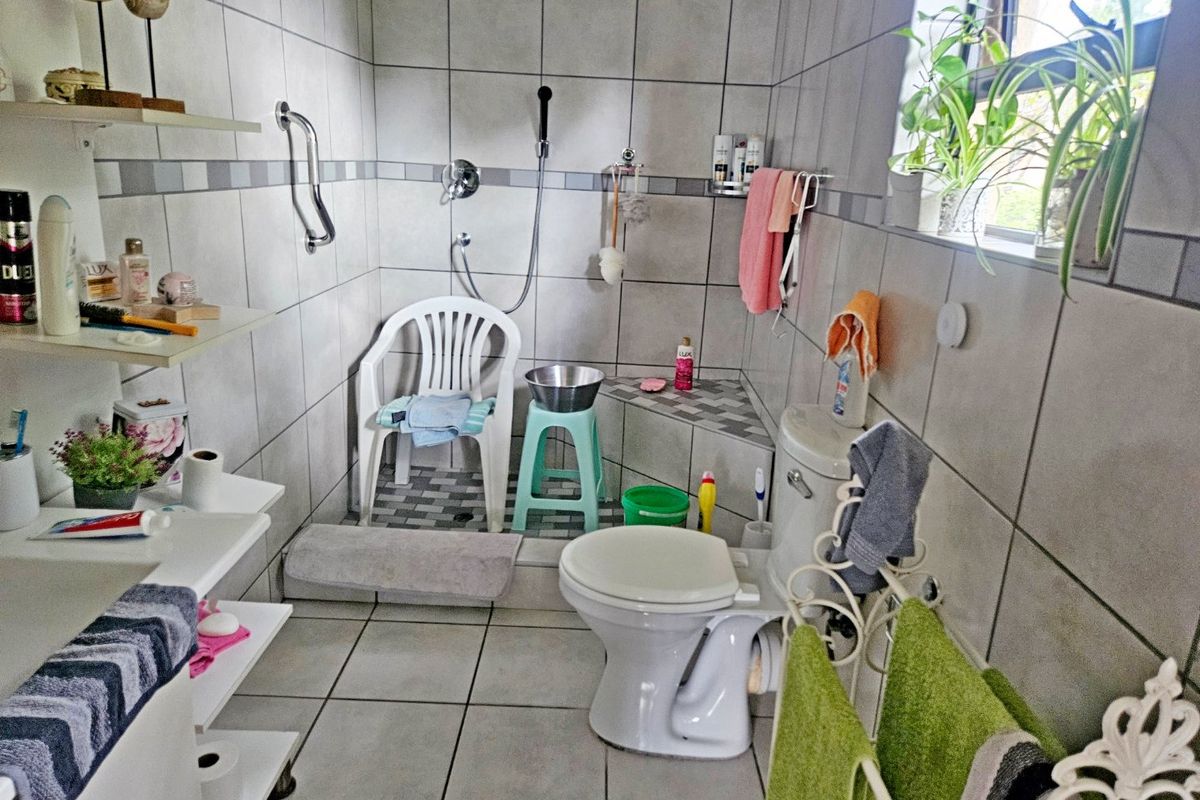 A functional bathroom featuring a walk-in shower with a grab rail, corner bench, and neutral ceramic tiling throughout.