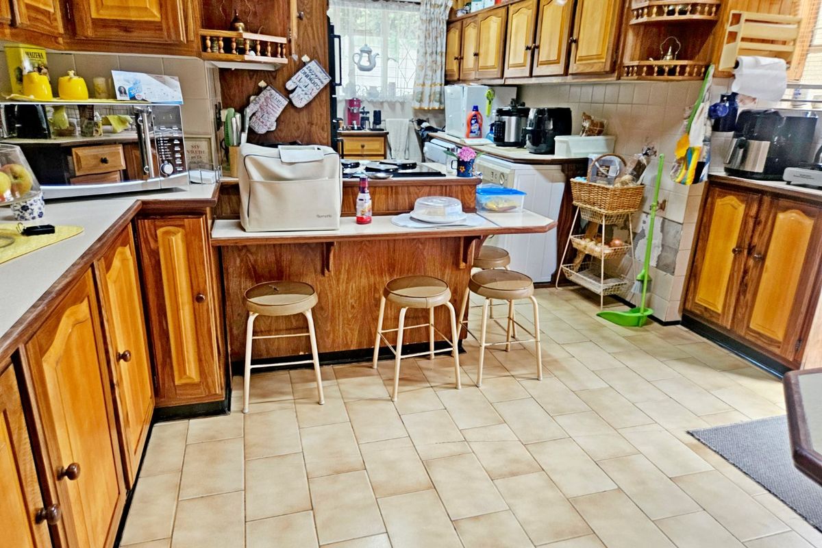 A dated kitchen featuring extensive wooden cabinetry, tiled flooring, and a breakfast bar, offering significant potential for a modern renovation.