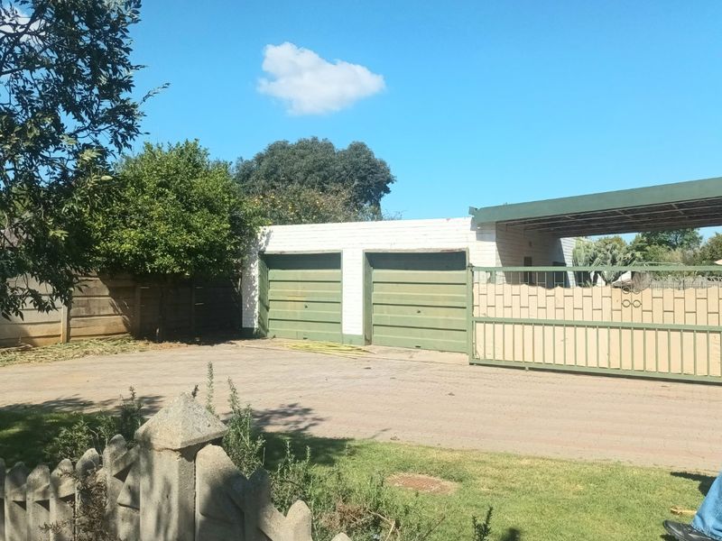 Exterior view of a double garage with an attached carport, paved driveway, and secure sliding gate entrance.