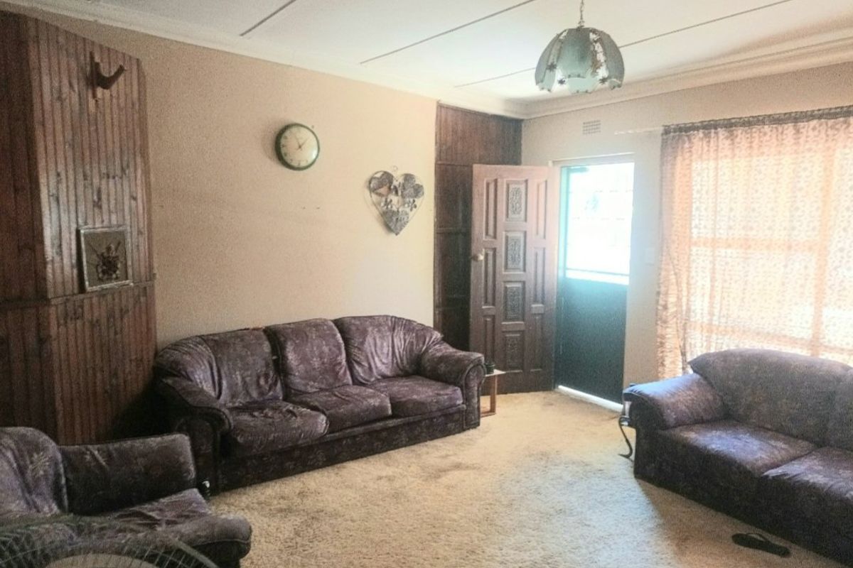 A living room featuring timber wall paneling, coved ceilings, and direct access to an exterior door, offering a dated interior space ready for modernization.