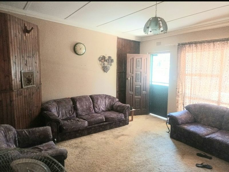 A living room featuring timber wall paneling, coved ceilings, and direct access to an exterior door, offering a dated interior space ready for modernization.