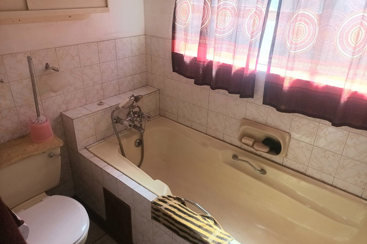 A dated bathroom featuring a built-in bathtub with wall-mounted mixer, tiled walls, and a standard toilet, offering potential for modernization.