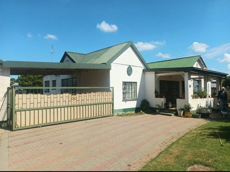 Front elevation of a single-story house featuring a paved driveway, sliding security gate, carport, and a covered entrance porch.