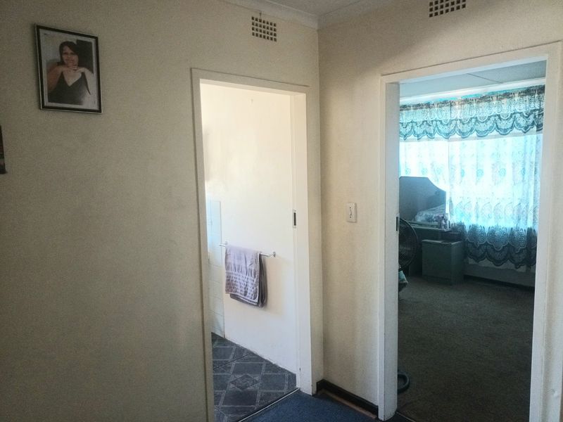 A functional hallway providing access to a bathroom and bedroom, featuring standard door frames and ventilation grilles.