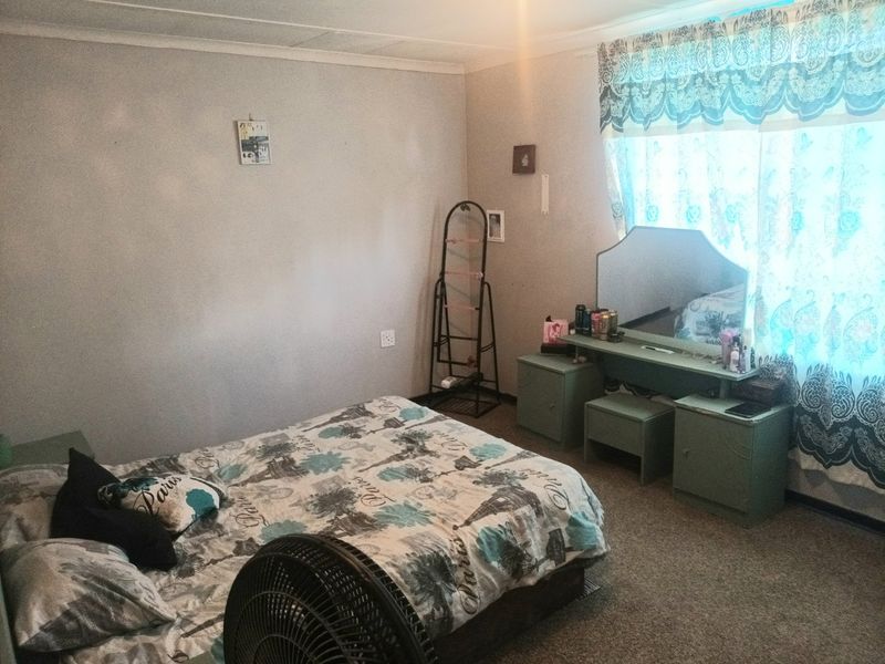 A standard bedroom featuring carpeted flooring and a large window with decorative curtains.