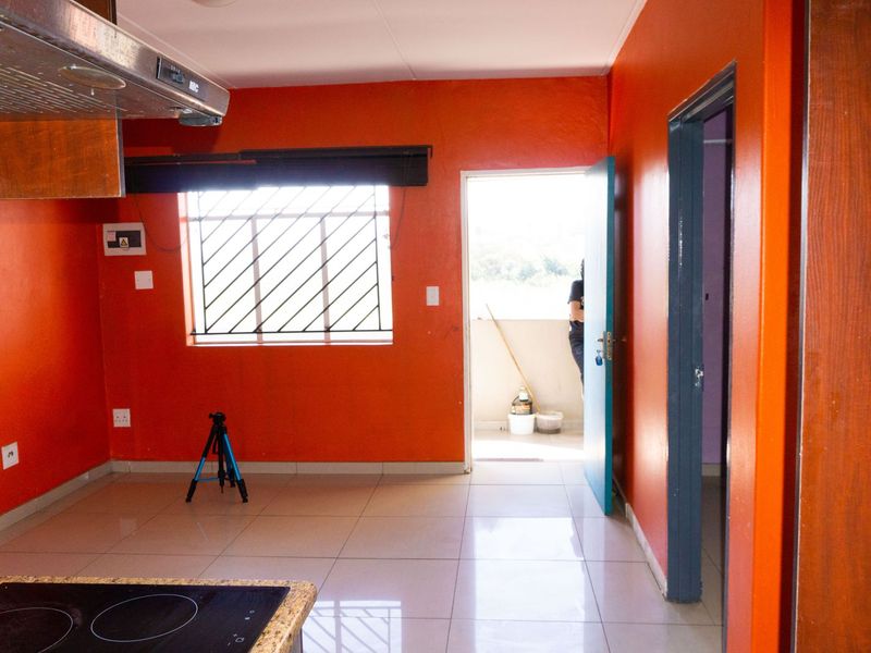 A functional kitchen area featuring tiled flooring, a built-in hob with extractor fan, and direct access to an outdoor balcony space.