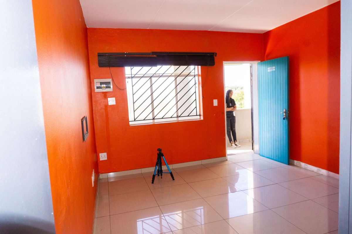 An empty bedroom featuring tiled flooring, bright orange walls, and a window with security bars, providing a blank canvas for personalization.