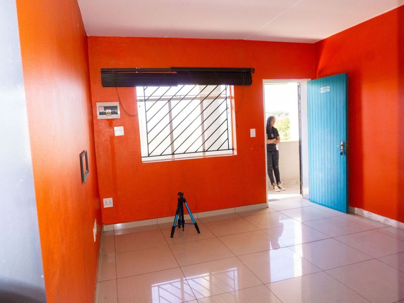 An empty bedroom featuring tiled flooring, bright orange walls, and a window with security bars, providing a blank canvas for personalization.