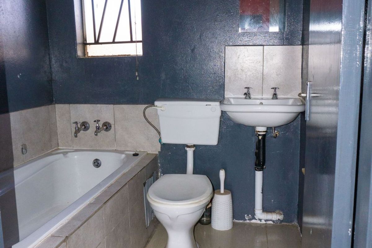 A compact bathroom featuring a bathtub, pedestal basin, and toilet, with tiled finishes and a window with security bars.