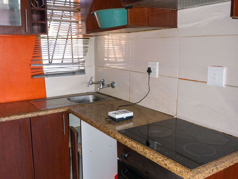 Compact kitchen featuring dark wood cabinetry, granite countertops, integrated oven and hob, and tiled backsplash, currently requiring minor repairs to cabinetry and flooring.