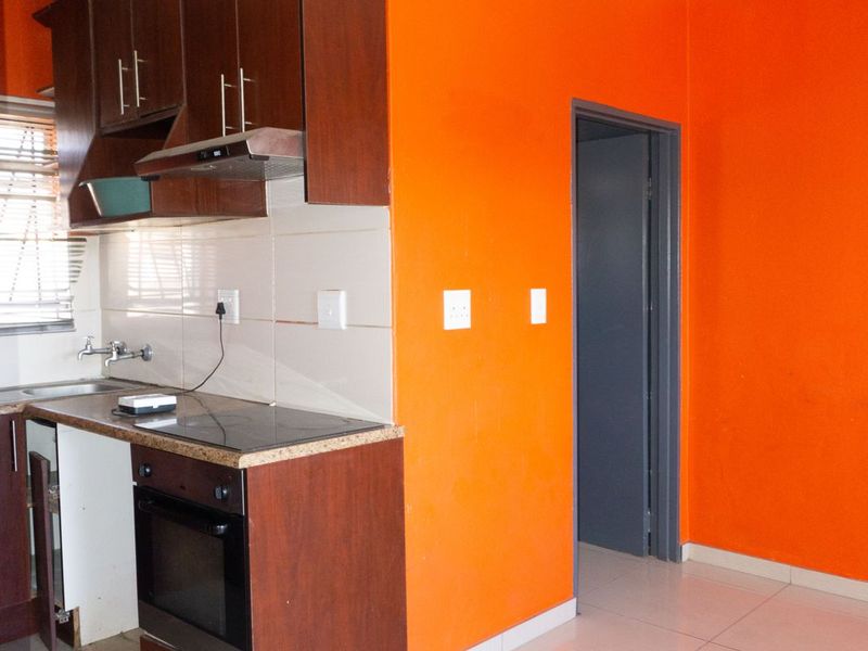 A compact kitchen featuring dark wood cabinetry, built-in oven and hob, tiled splashback, and bright orange accent walls.