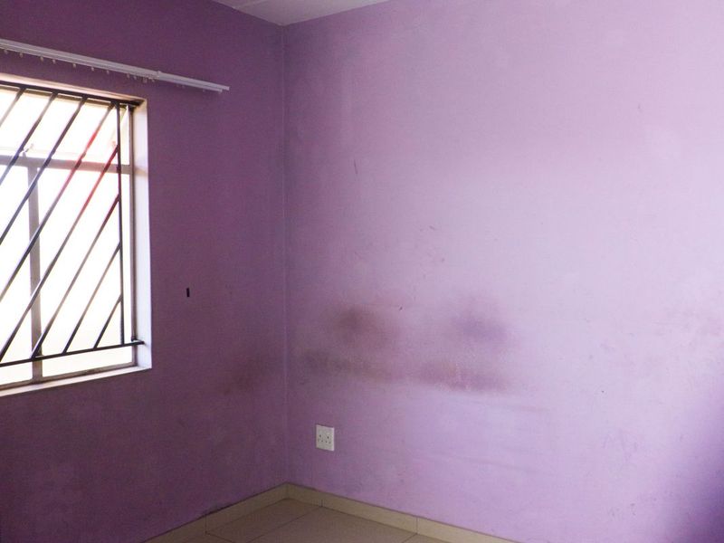 An empty bedroom featuring tiled flooring, security bars on the window, and a ceiling light fixture, requiring cosmetic updates to the wall finishes.