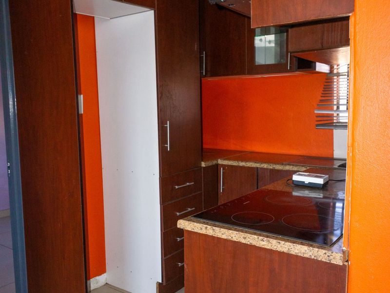 A compact kitchen featuring dark wood-look cabinetry, laminate countertops, an integrated electric hob, and an extractor fan with bright orange accent walls.