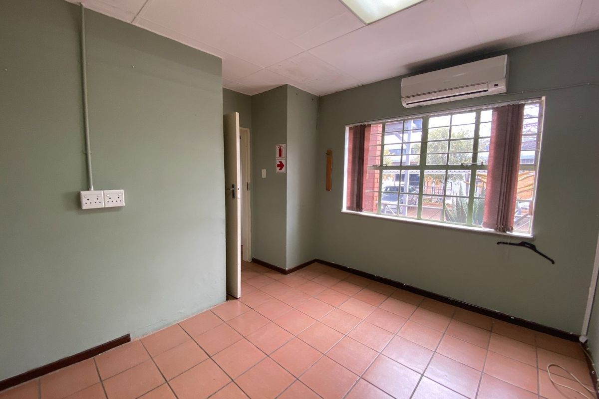 A functional, empty office space featuring tiled flooring, a drop ceiling with integrated lighting, and a wall-mounted air conditioning unit.