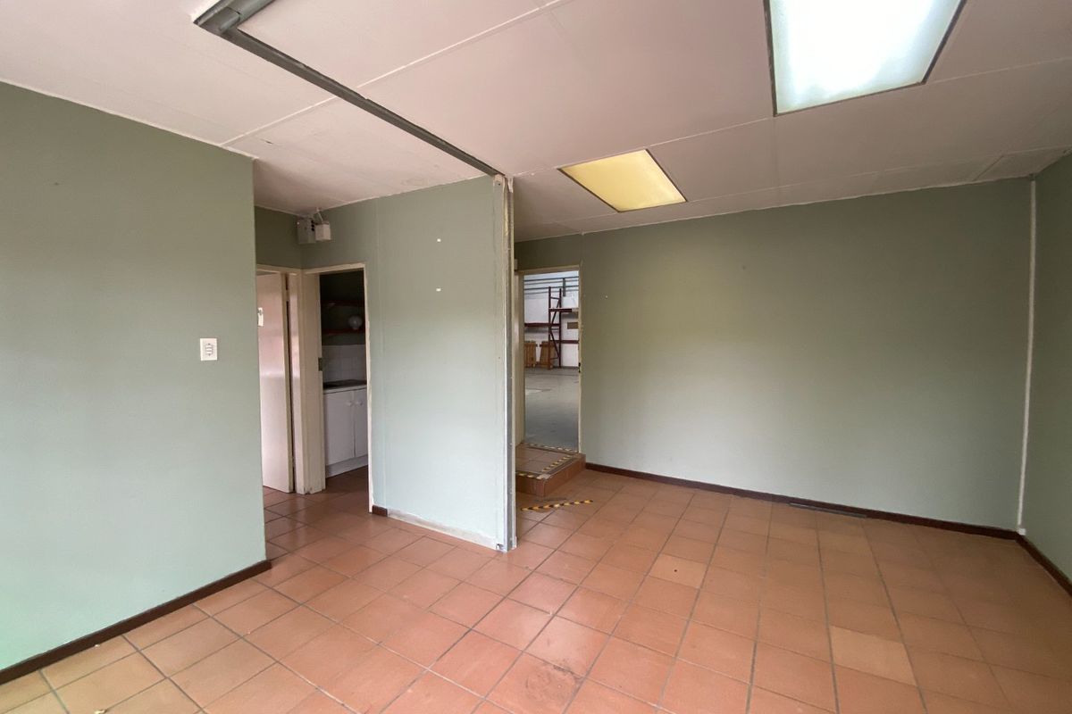 An empty office space featuring ceramic tile flooring, suspended ceiling with recessed lighting, and a partition wall leading to adjacent utility areas.