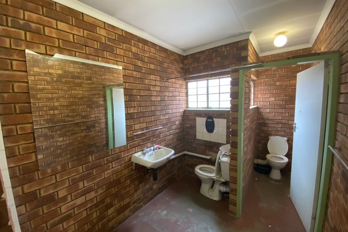Industrial-style bathroom featuring exposed brick walls, two toilets, and a wall-mounted basin, requiring cosmetic updates to improve functionality and aesthetic appeal.