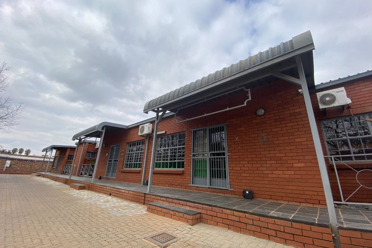 Exterior view of an industrial property featuring a face brick facade, metal awnings, paved driveway, and secure access points with security gates.