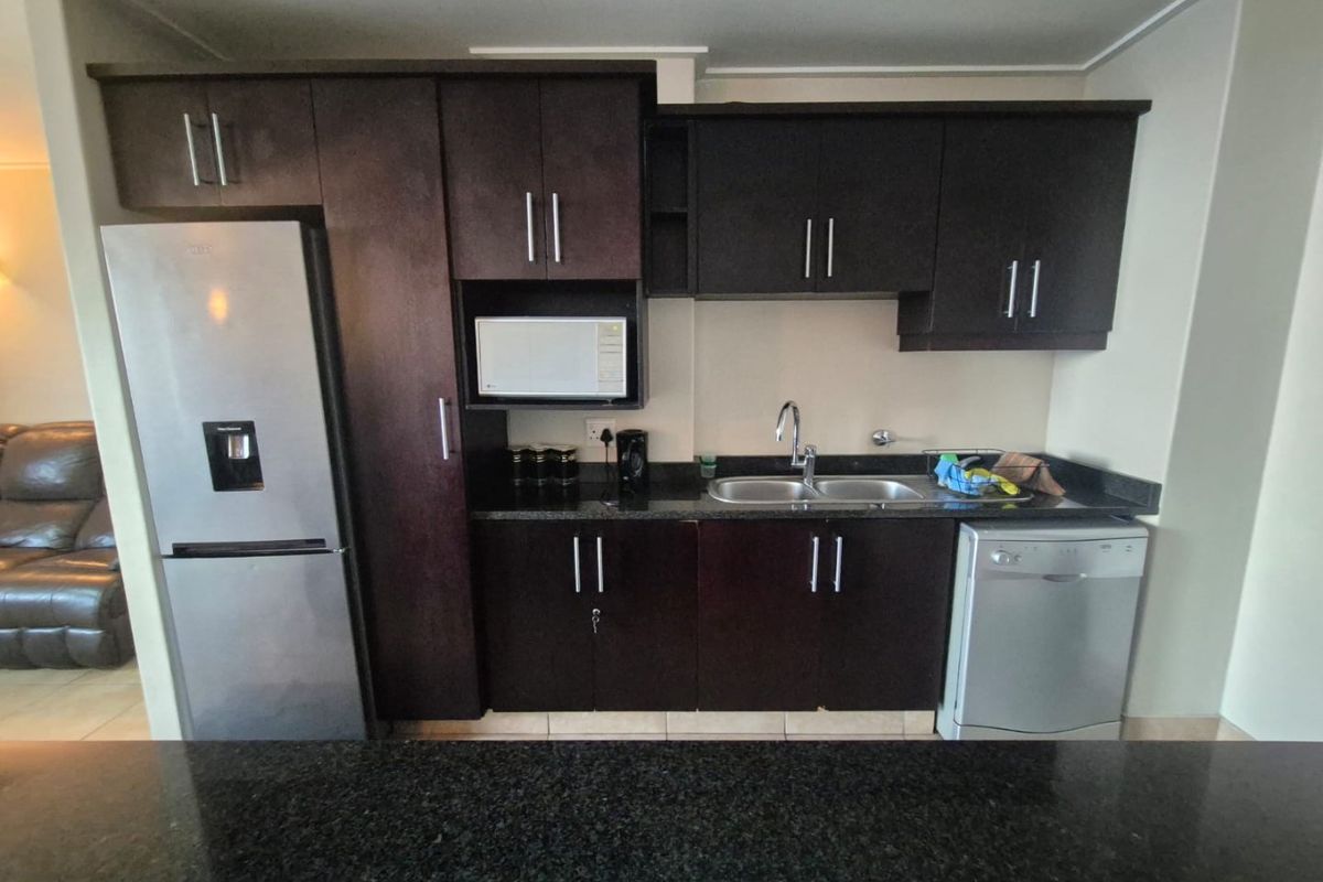 A functional kitchen featuring dark wood cabinetry, granite countertops, a double basin sink, and built-in microwave space.