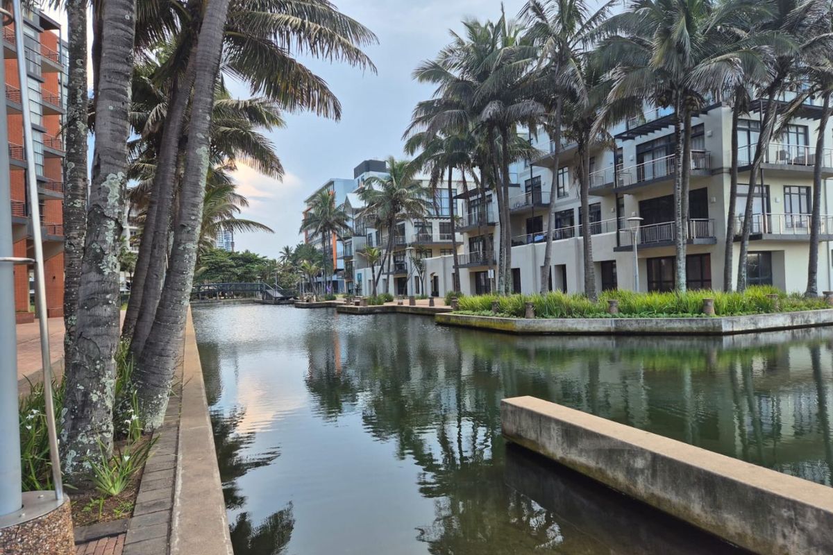 A scenic view of the apartment complex exterior featuring a canal, landscaped gardens, and private balconies overlooking the water.