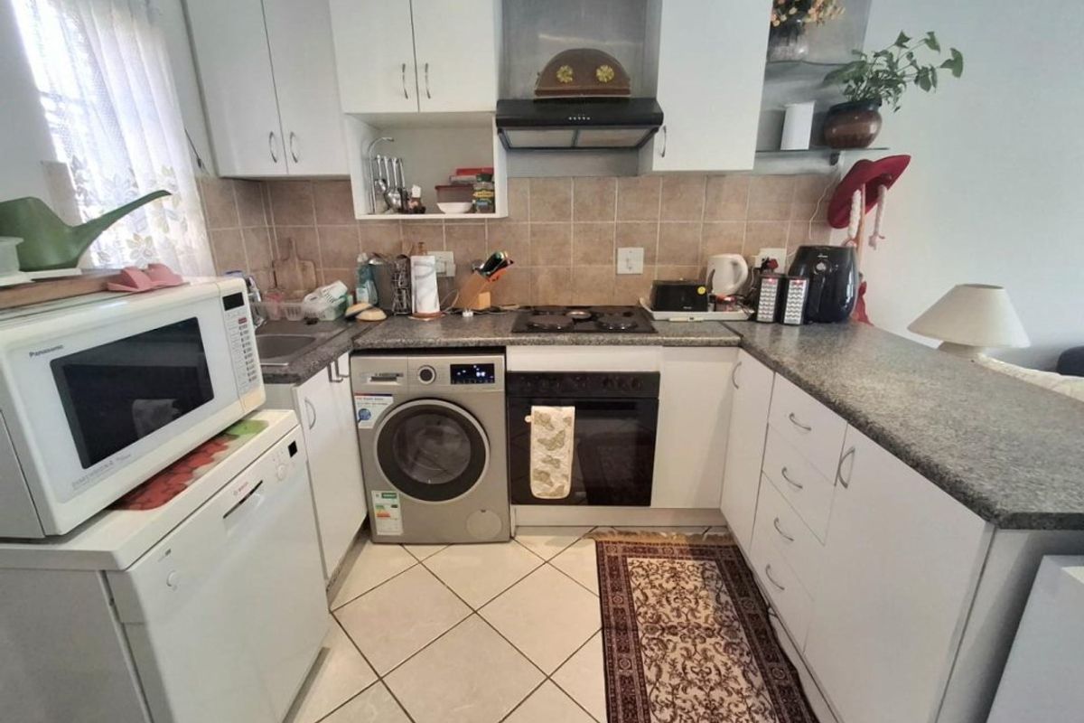 Compact kitchen featuring white cabinetry, granite countertops, tiled backsplash, and built-in appliances including an oven, hob, and extractor fan.