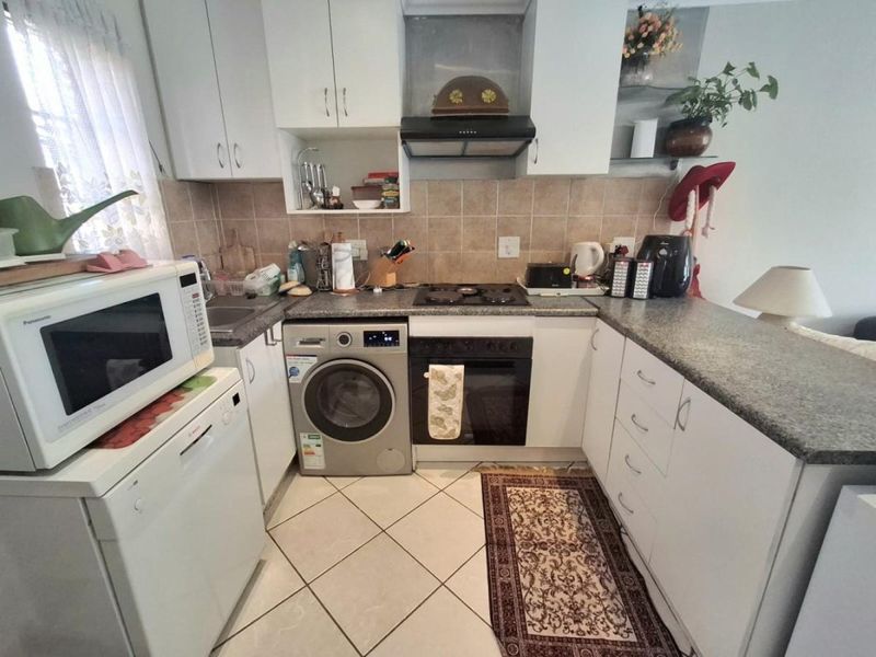 Compact kitchen featuring white cabinetry, granite countertops, tiled backsplash, and built-in appliances including an oven, hob, and extractor fan.