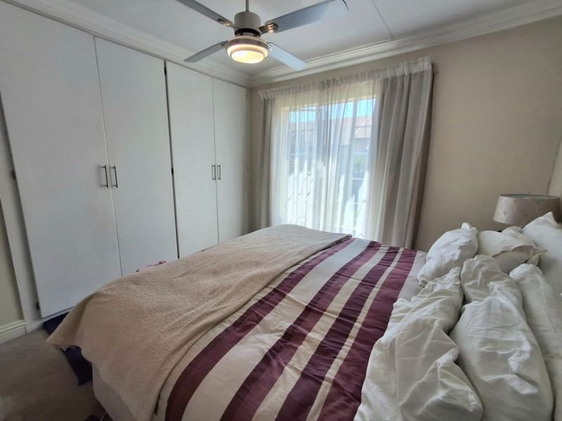 A well-maintained bedroom featuring floor-to-ceiling built-in cupboards, a central ceiling fan, and large windows with sheer curtains allowing natural light.