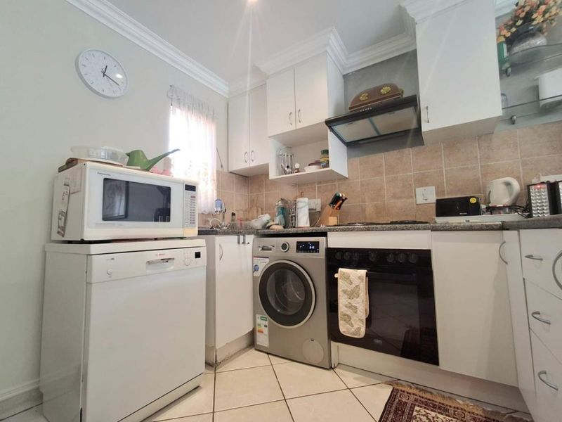 A functional kitchen featuring white cabinetry, granite countertops, tiled backsplash, and integrated appliances including an oven, hob, and extractor fan.