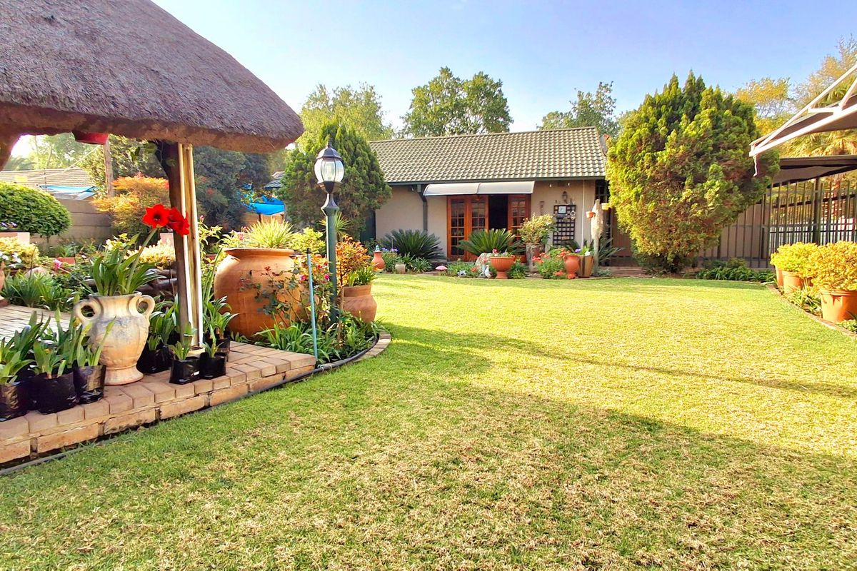 A well-maintained rear garden featuring a thatched lapa, manicured lawn, and established landscaping leading to the main dwelling.