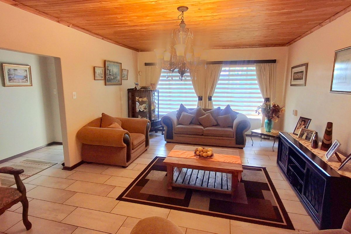 A spacious living room featuring a warm timber tongue and groove ceiling, neutral ceramic floor tiles, and a classic chandelier.
